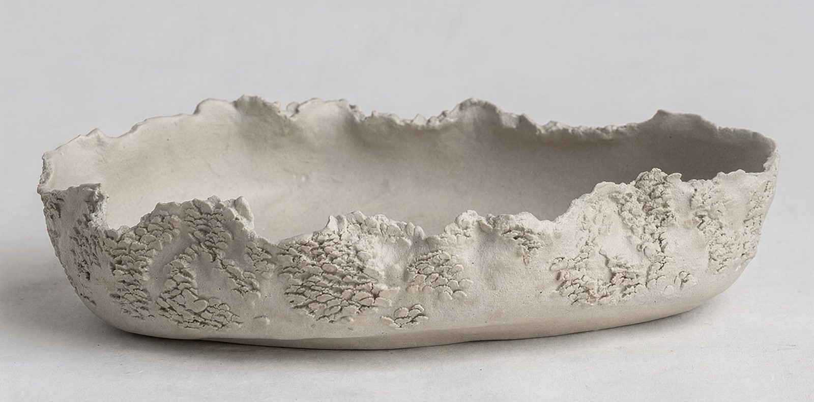 Wide hand-built ceramic vessel with a torn rim and heavily encrusted lower surface in cream stoneware, by Consuelo Becerra