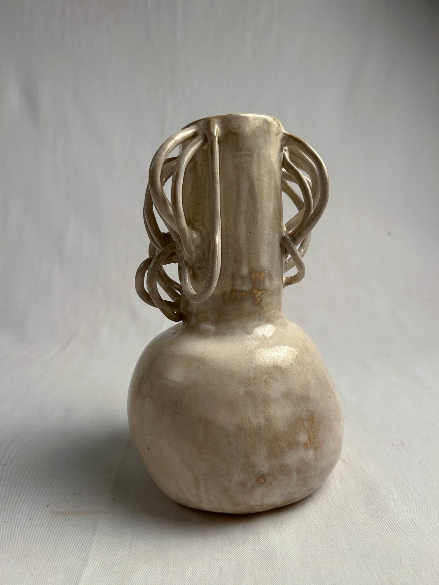 Hand-built ceramic bottle with a nest of coiled handles around the neck and a pale glossy glaze, by Consuelo Becerra