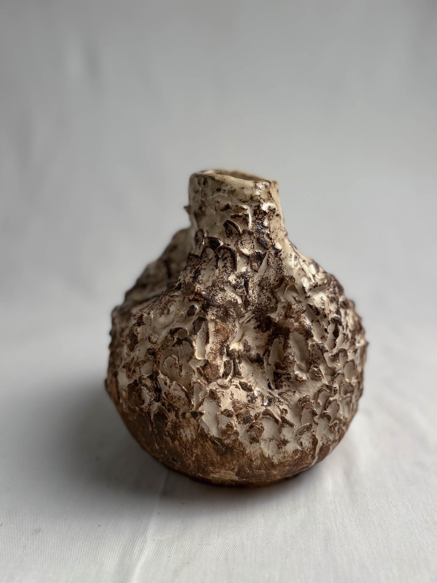 Round hand-built ceramic vessel with an encrusted textured surface in earth tones, by Consuelo Becerra