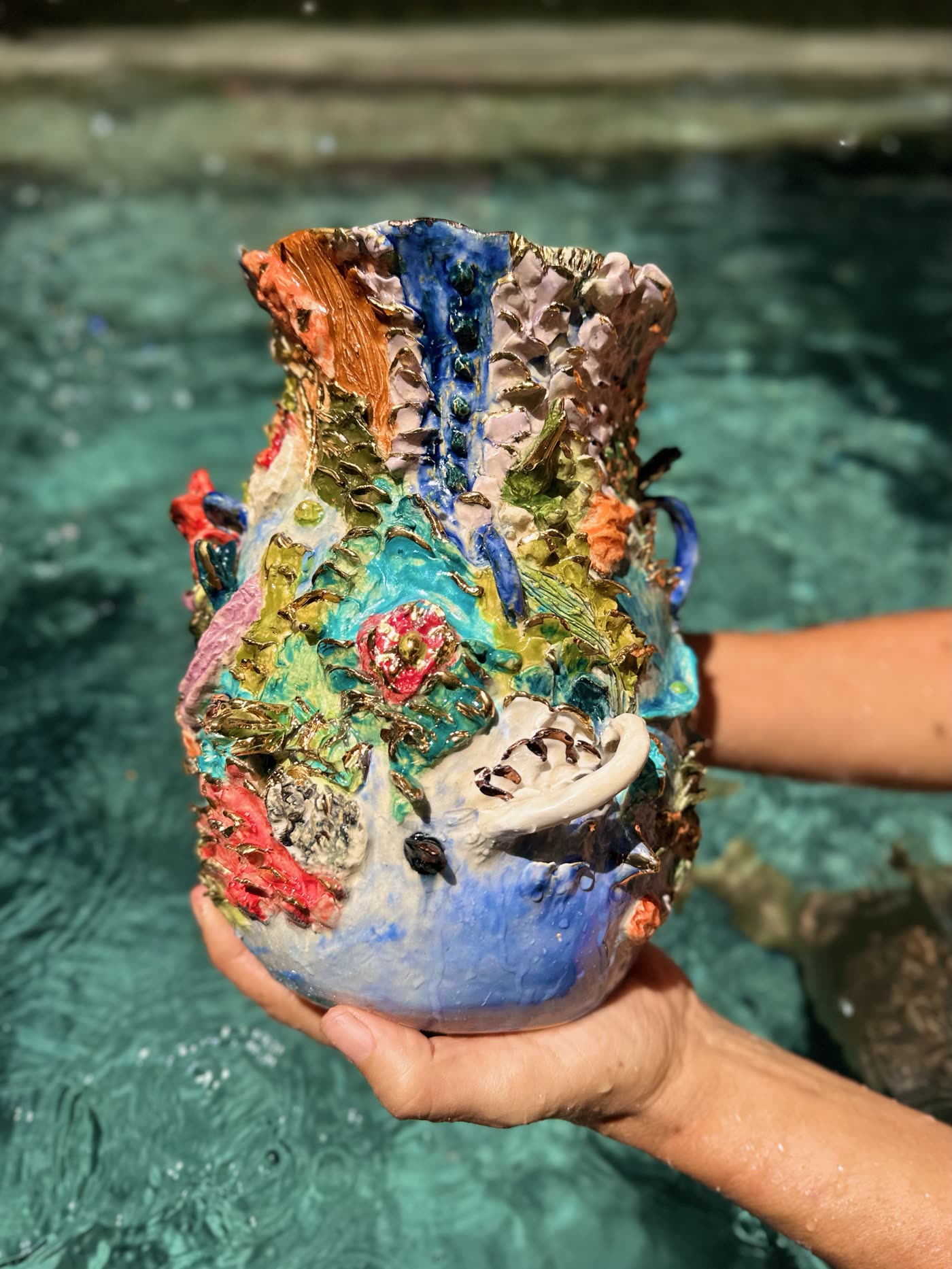 Coral reef ceramic vessel by Consuelo Becerra held over turquoise water, showing the blue glazed base, view 3 of 5