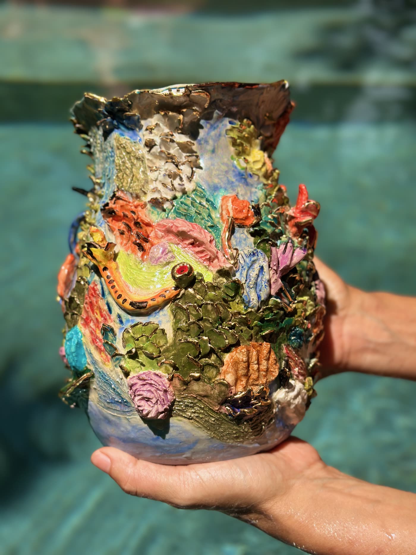 Hand-built ceramic vessel encrusted with a polychrome coral reef in relief, held above a swimming pool, by Consuelo Becerra, view 1 of 5