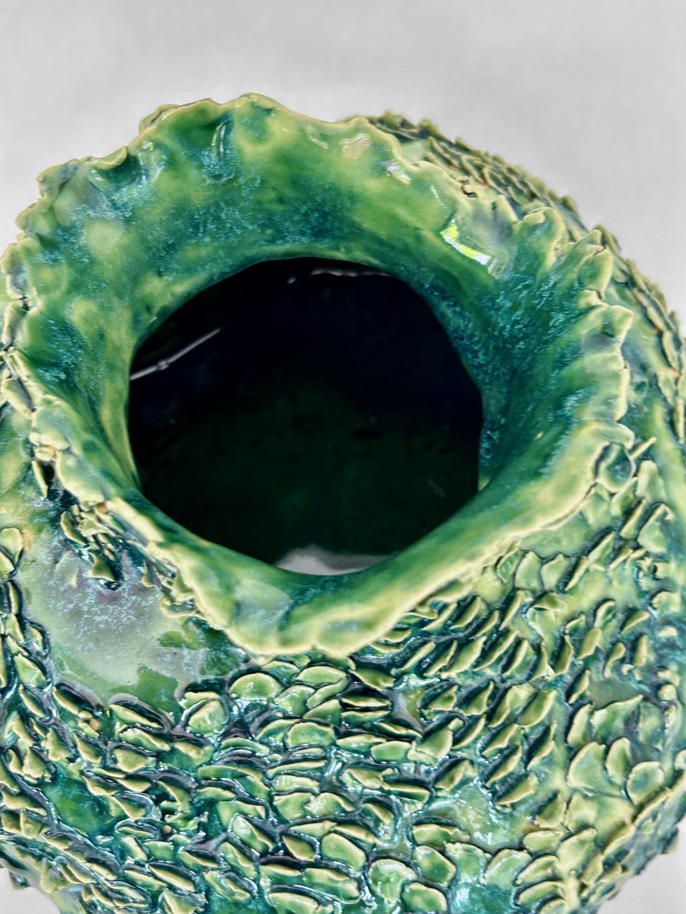 Close view into the mouth of the scaled green vessel by Consuelo Becerra, showing the pooled glaze inside the rim, view 2 of 6