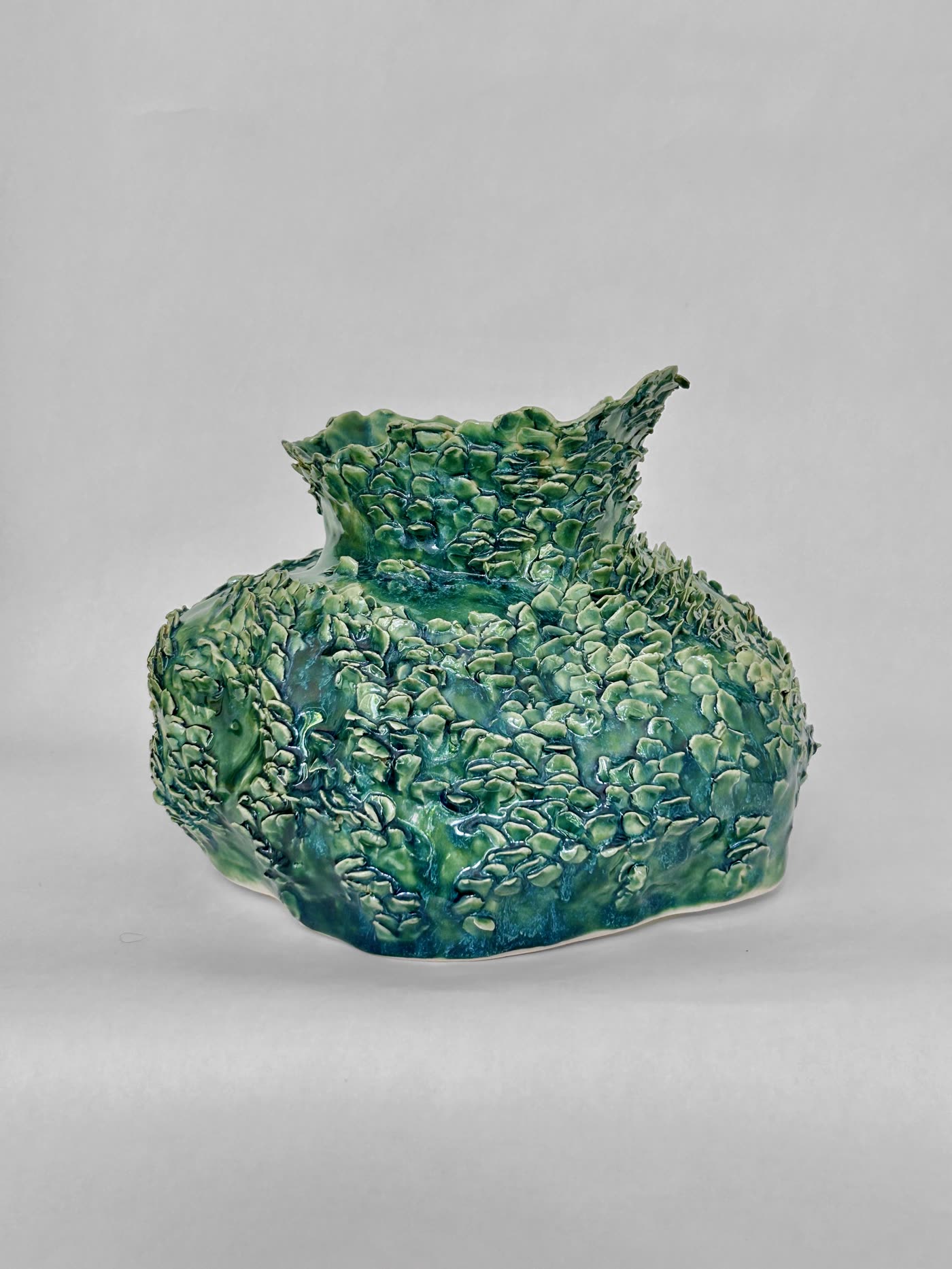 Squat hand-built ceramic vessel with a torn flared rim, covered in overlapping scale-like nubs in mottled green and teal glaze, by Consuelo Becerra, view 1 of 6