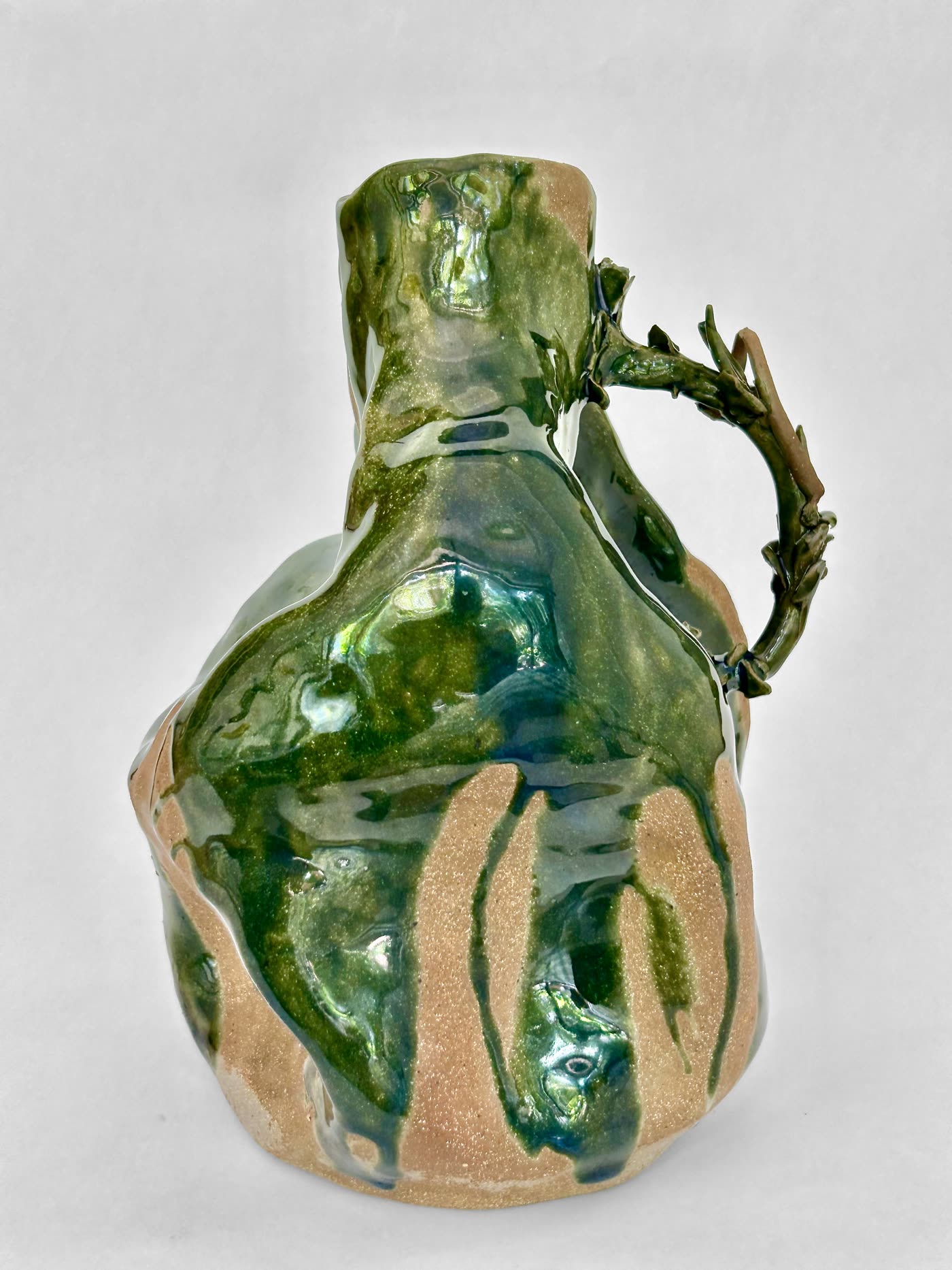 Hand-built ceramic jar with a branch-like modelled handle arching from neck to shoulder, green glazes running over exposed buff stoneware, by Consuelo Becerra, view 1 of 4