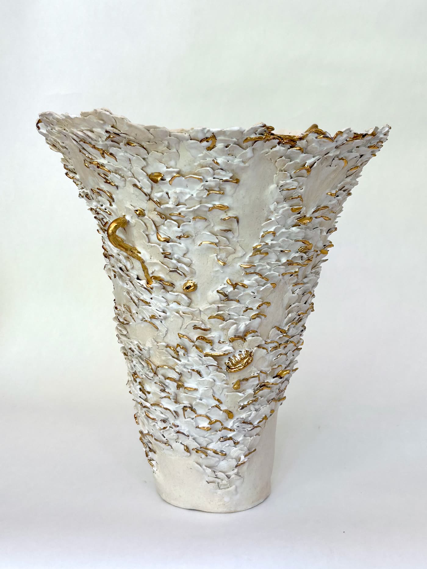 Tall hand-built ceramic vessel flaring wide at the mouth from a narrow foot, its surface covered in applied petal-like fragments in white glaze with gold lustre highlights, by Consuelo Becerra, view 1 of 8