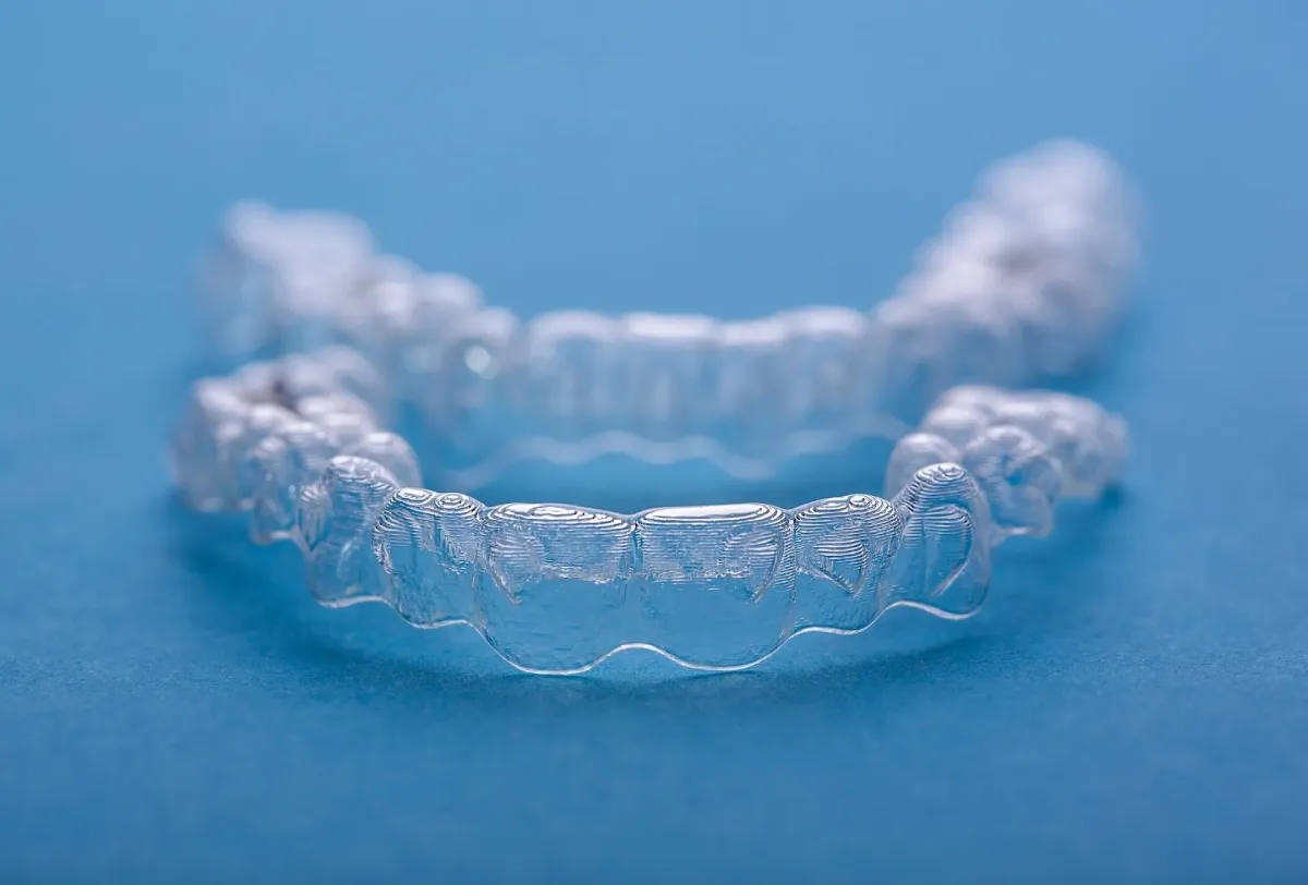 Clear removable dental aligner rests on a blue surface in close-up, with a blurred second aligner behind it, creating a clean clinical tone.