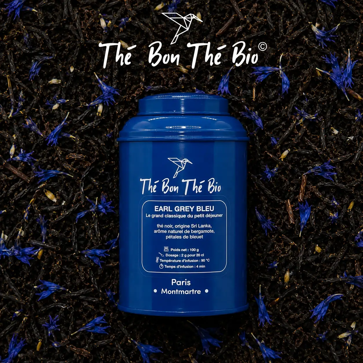 Boîte bleue de thé noir Earl Grey Bleu de la marque Thé Bon Thé Bio posée sur un fond de feuilles de thé noir avec des pétales de bleuet, indiquant l'origine Sri Lanka, arôme naturel de bergamote, poids net 100g et instructions d'infusion.