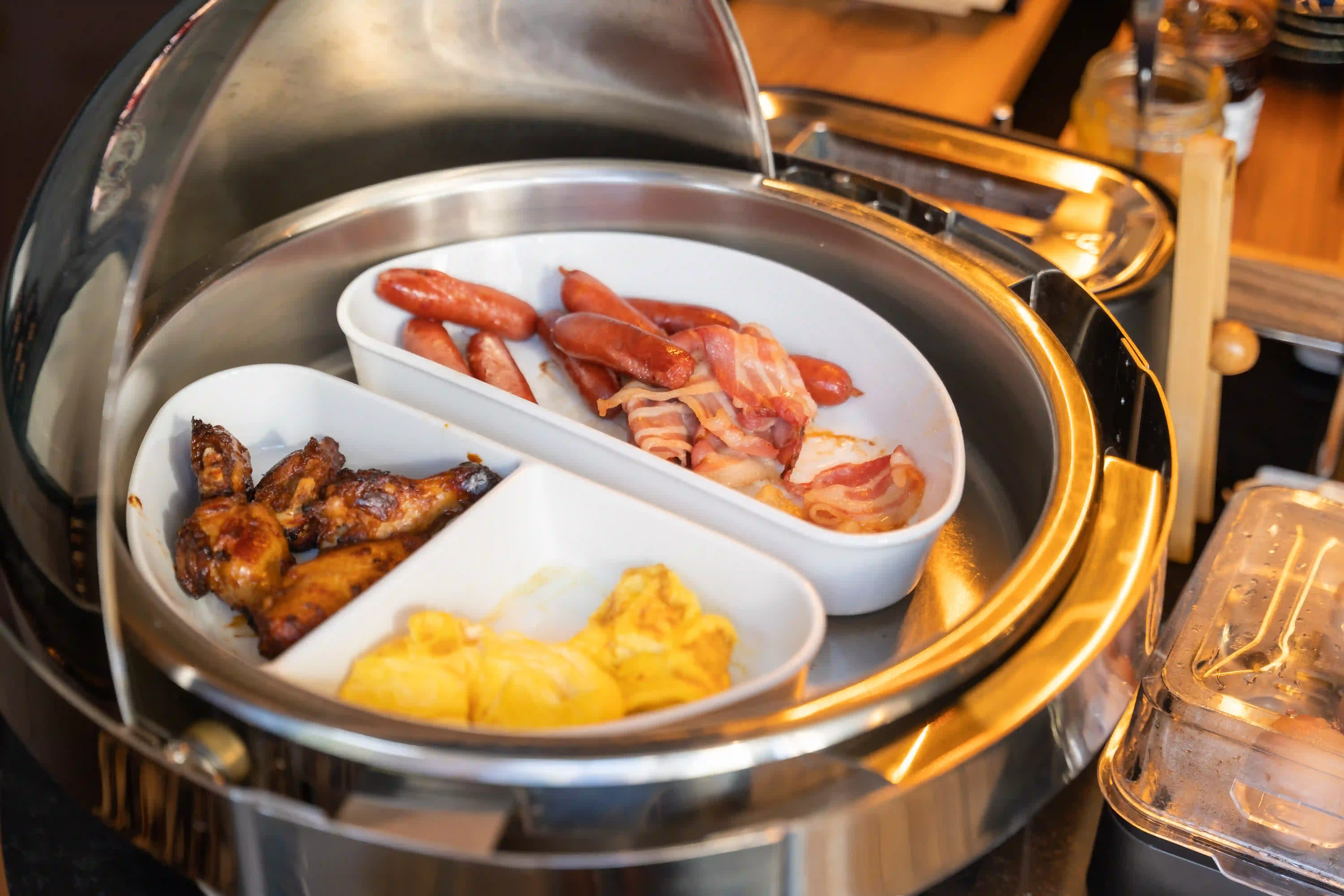 Warme Platte mit Würstchen, Speck, gegrillten Hähnchenflügeln und Rührei an einem Buffet