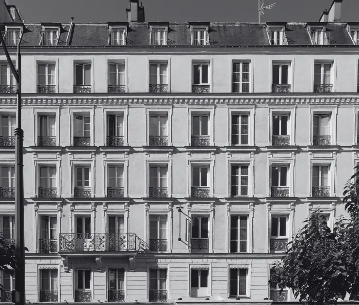 Façade d'un immeuble parisien classique avec cinq étages de fenêtres alignées et balcons en fer forgé, en noir et blanc.