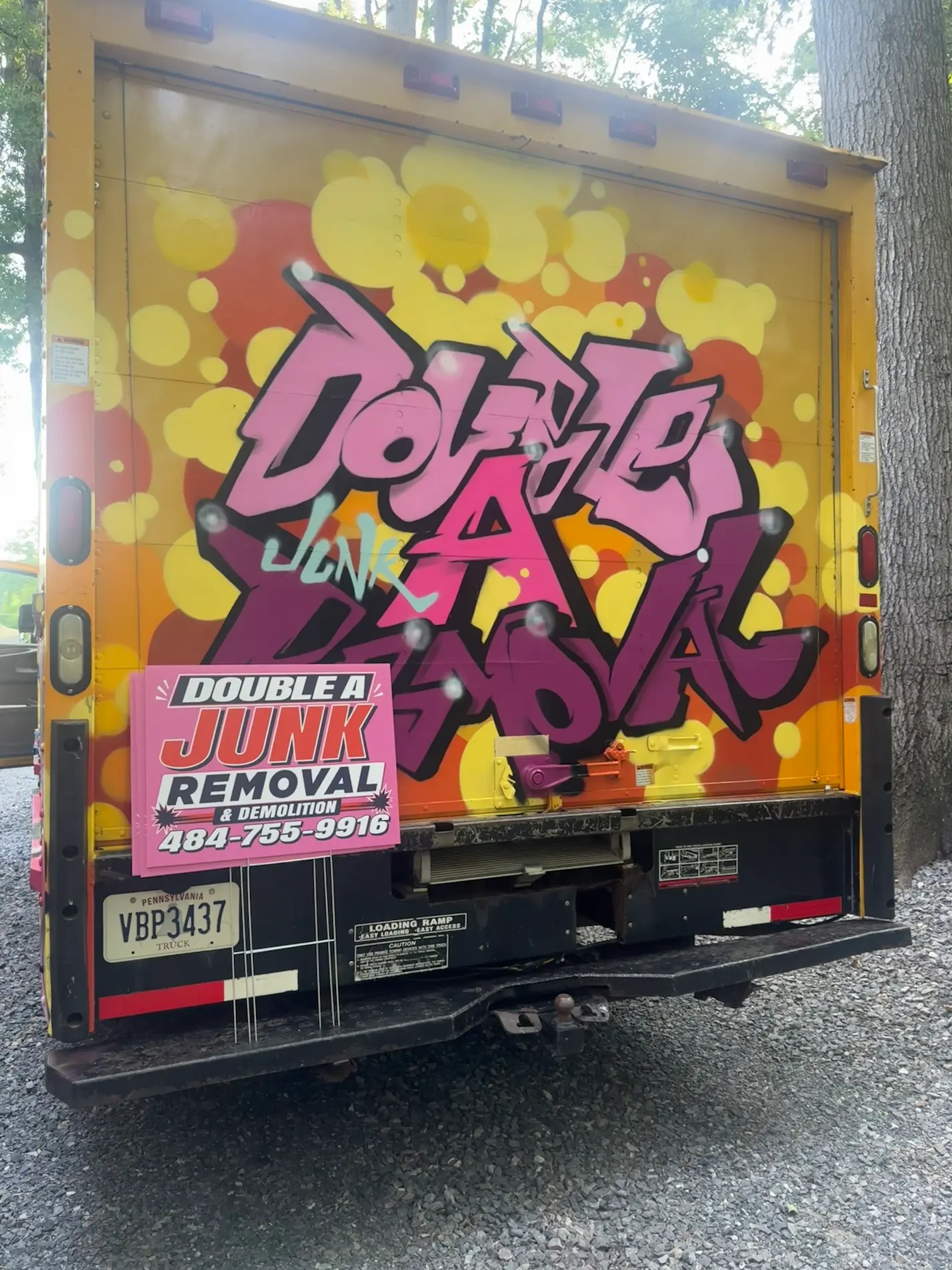 Back of a truck with colorful graffiti reading 'Double A Junk' and a sign in front advertising Double A Junk Removal & Demolition with phone number 484-755-9916 and Pennsylvania license plate VBP3437.
