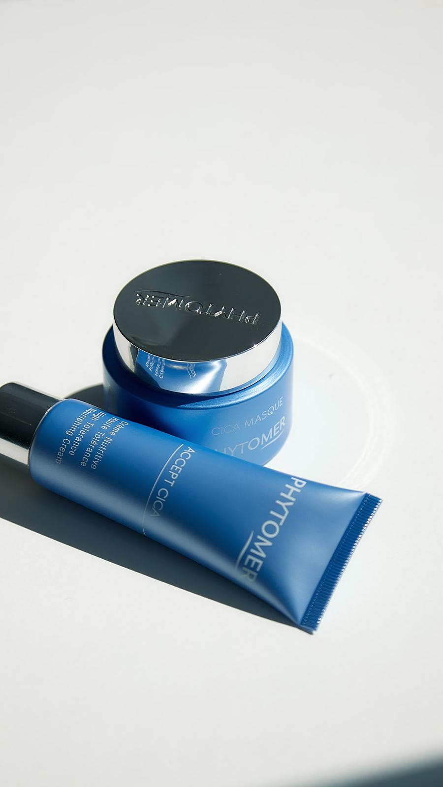 Two blue skincare products by Phytomer on a white surface, including a jar labeled Cica Masque and a tube labeled Accept Cica Nutrient High Tolerance Soothing Cream.