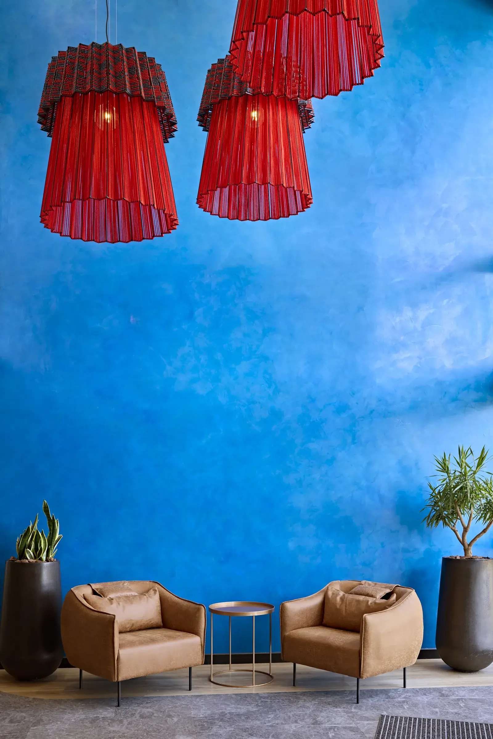 A sculptural red pendant installation against a deep blue wall, a detail from a Design Partnership interior.