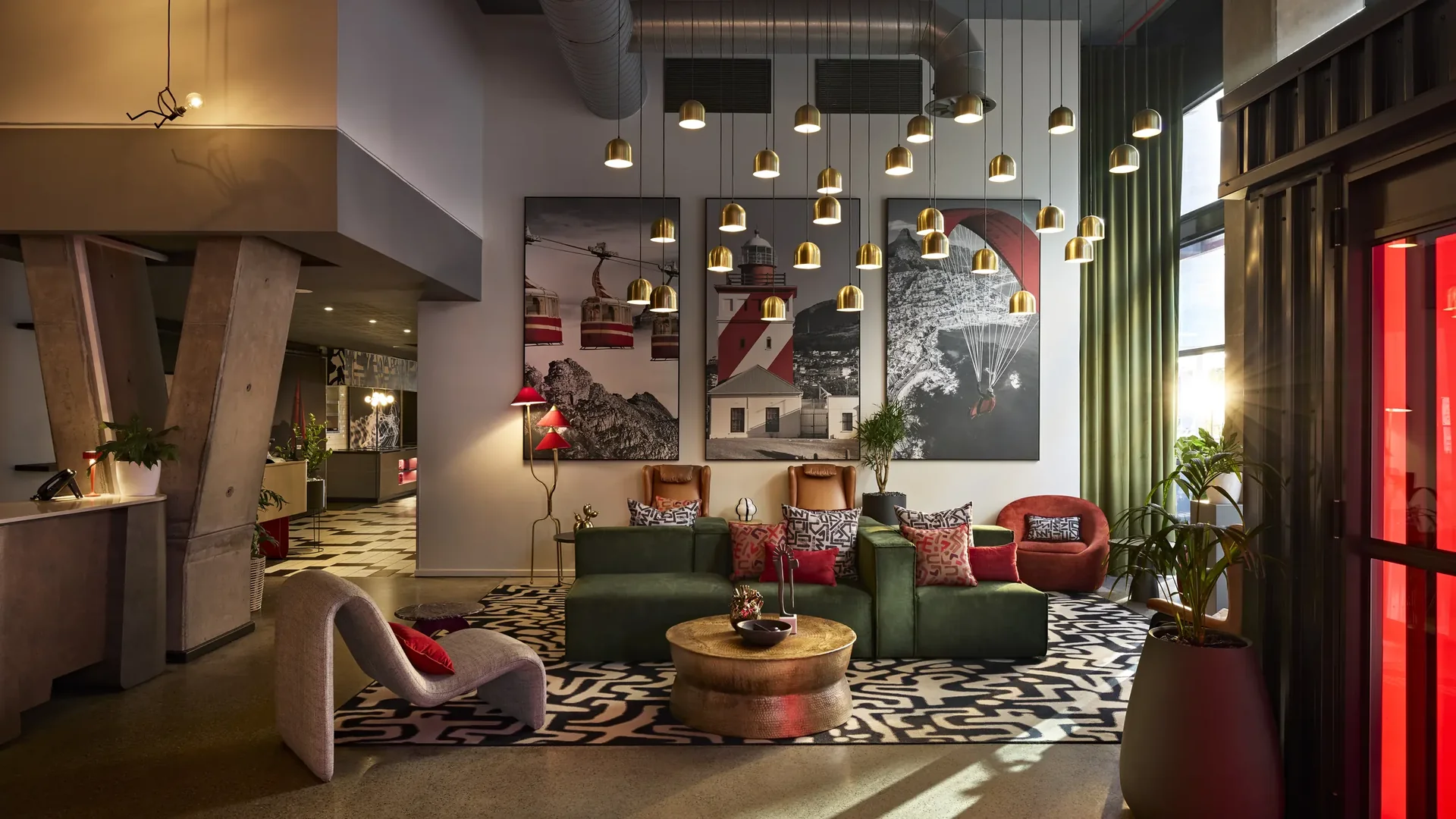 Hotel lobby lounge with green velvet seating, a cluster of brass pendants and bold gallery artwork, designed and built by Design Partnership.