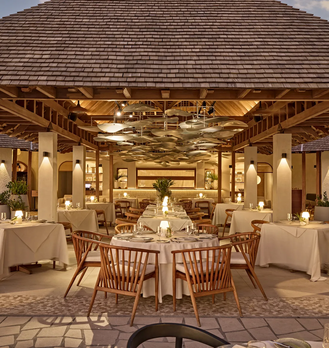 Thatched pavilion restaurant interior design in Mauritius with candlelit round tables and cane dining chairs beneath an exposed timber roof.