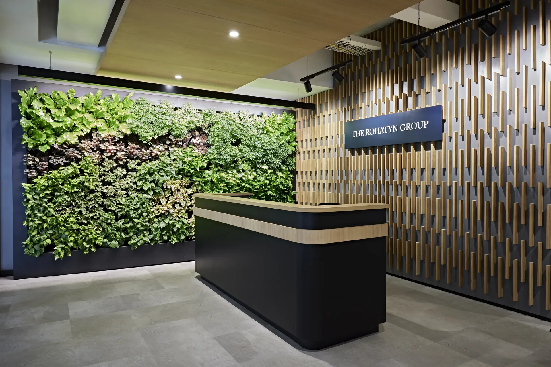 The Rohatyn Group reception with a full-height living green wall, timber batten screen and a dark stone welcome desk, designed and built by Design Partnership in Johannesburg.