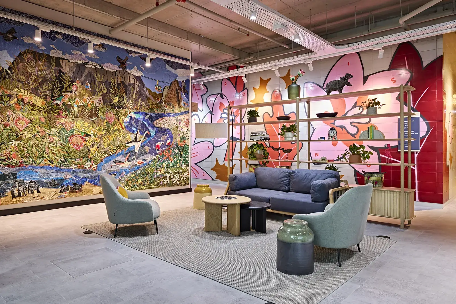 Workplace breakout lounge with a full-height painted mural, soft seating and sculptural side tables. Workplace design and built by Design Partnership.