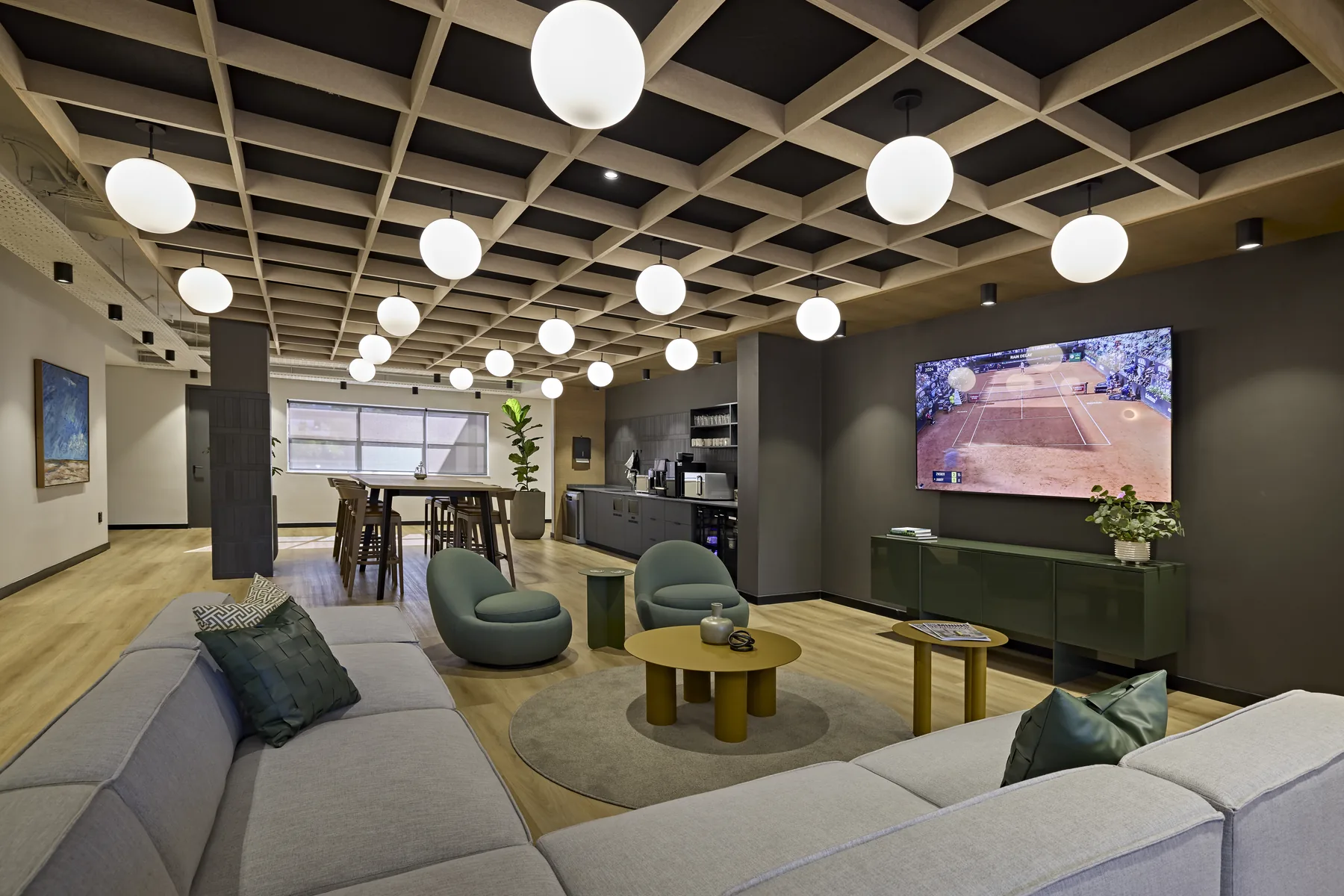 Workplace lounge with a timber coffered ceiling, globe pendants, green armchairs and a modular sofa. Corporate office interior designed and built by Design Partnership.