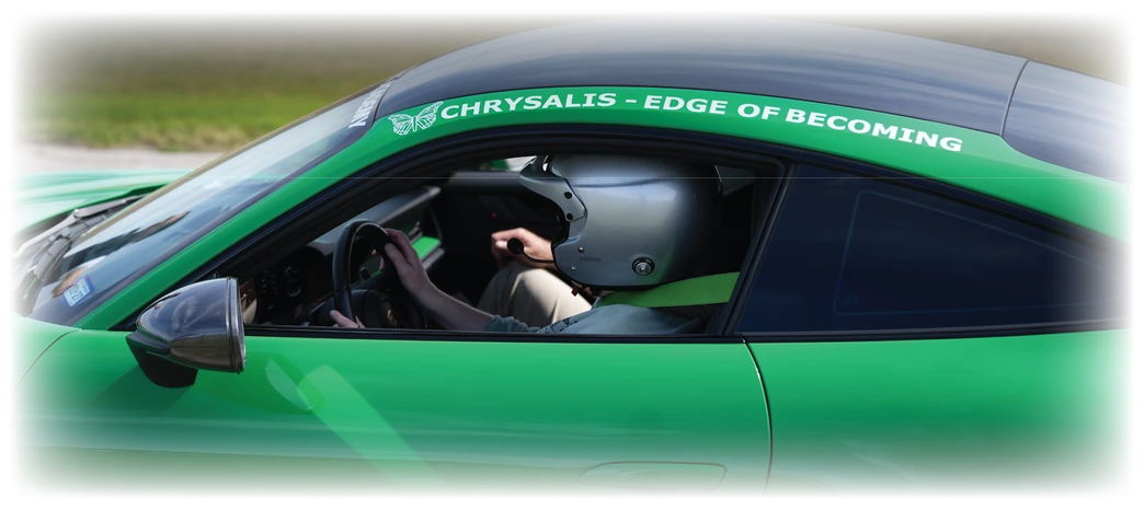 Driver at the wheel of the green Porsche, windscreen banner reading Chrysalis — Edge of Becoming