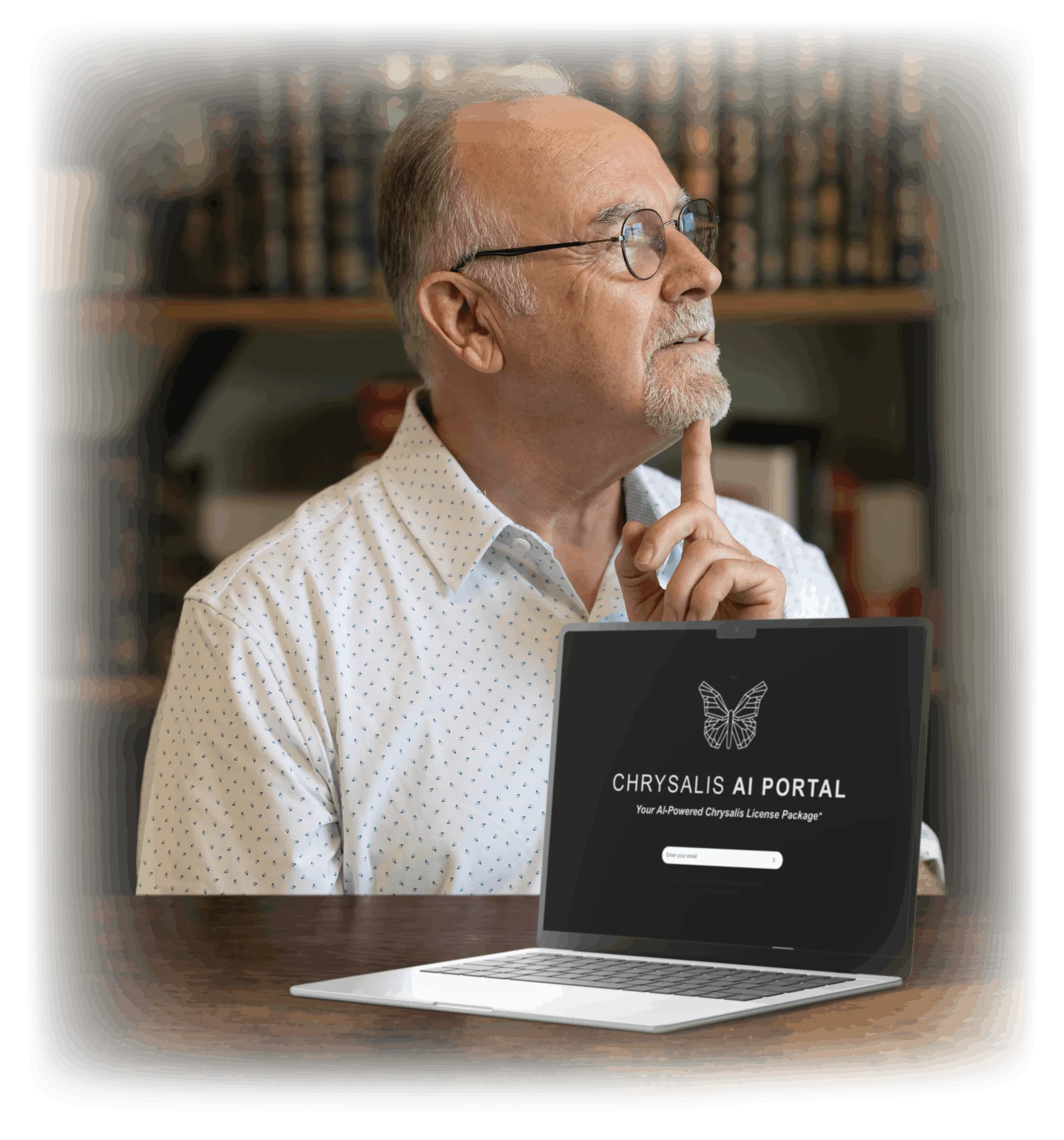 Ron J West seated at a desk in thought beside a laptop showing the Chrysalis AI Portal