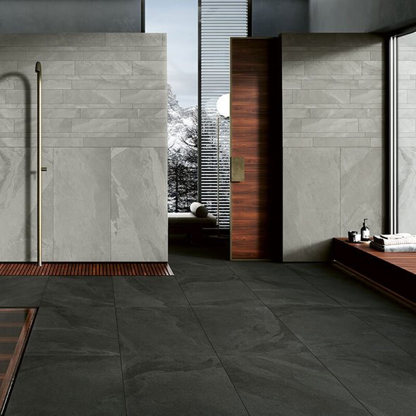 Modern bathroom with slate flooring, light gray tile walls, wooden accents, and dark wooden door.