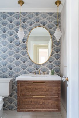 Modern bathroom with blue patterned wallpaper, wooden vanity, and oval gold-framed mirror