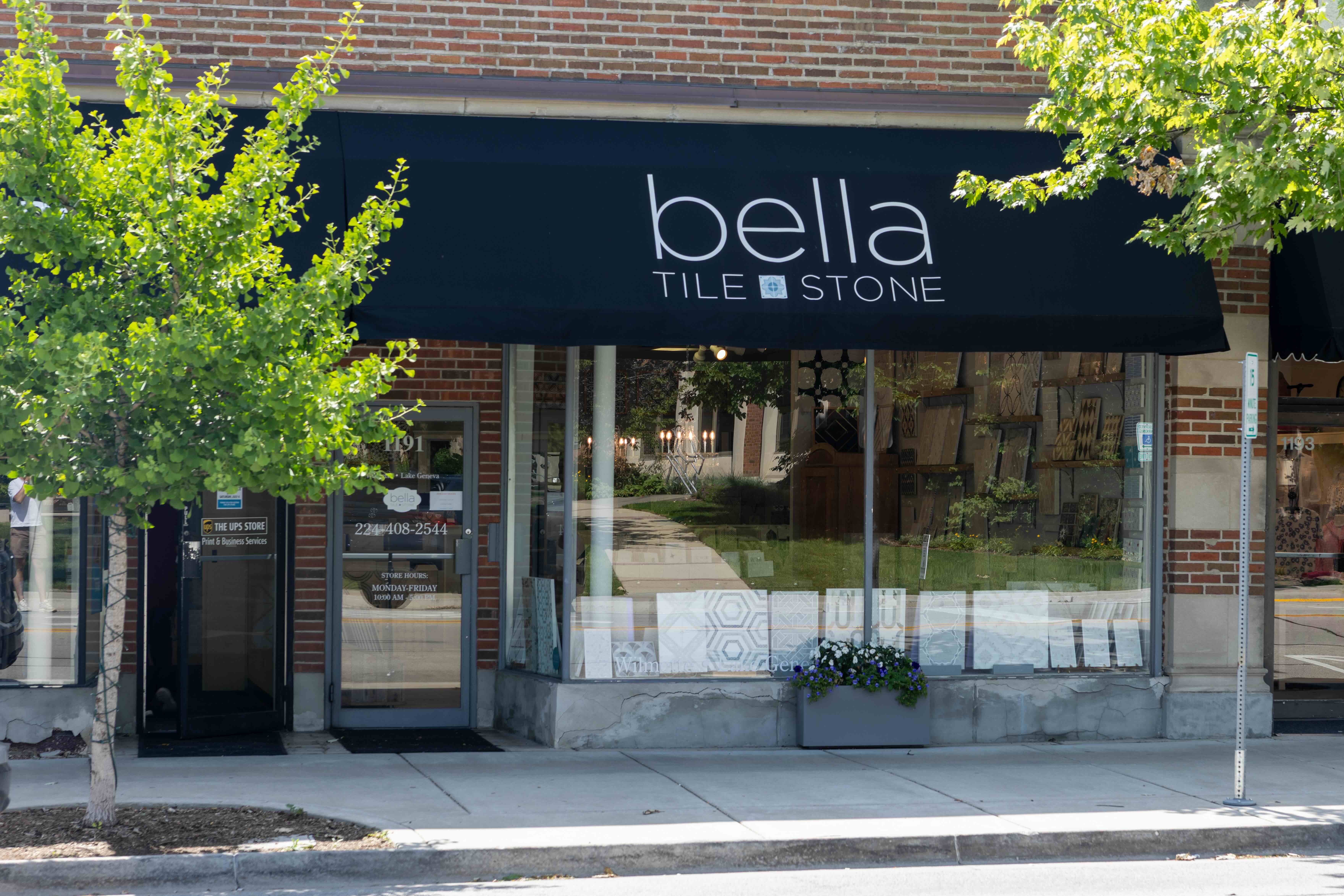 Bella Tile and Stone storefront with dark awning, brick facade, and green ivy foliage.