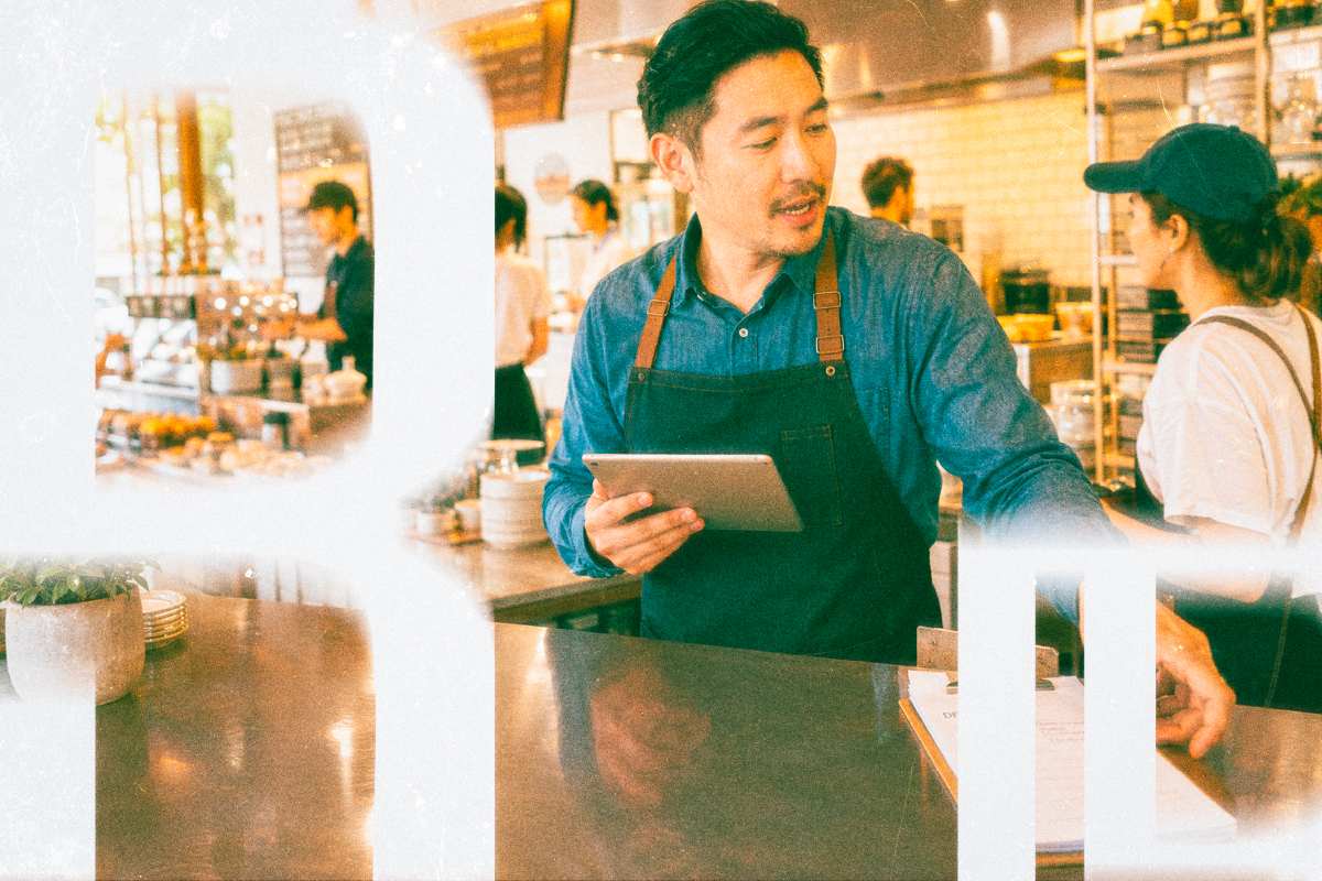 Cafe manager holding a tablet in a busy kitchen.