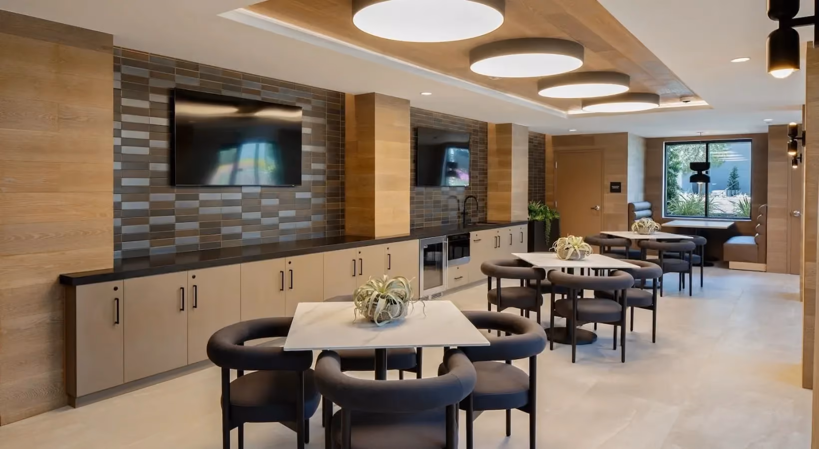 Community lounge area with extended black countertop, built-in appliances, and two mounted TVs