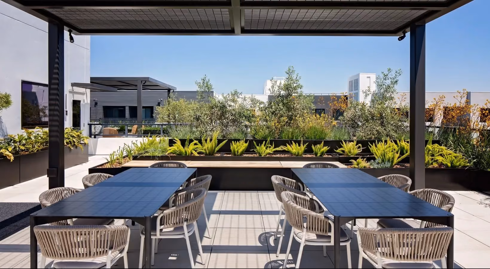 Rooftop gathering space with large tables, seating, and landscaping