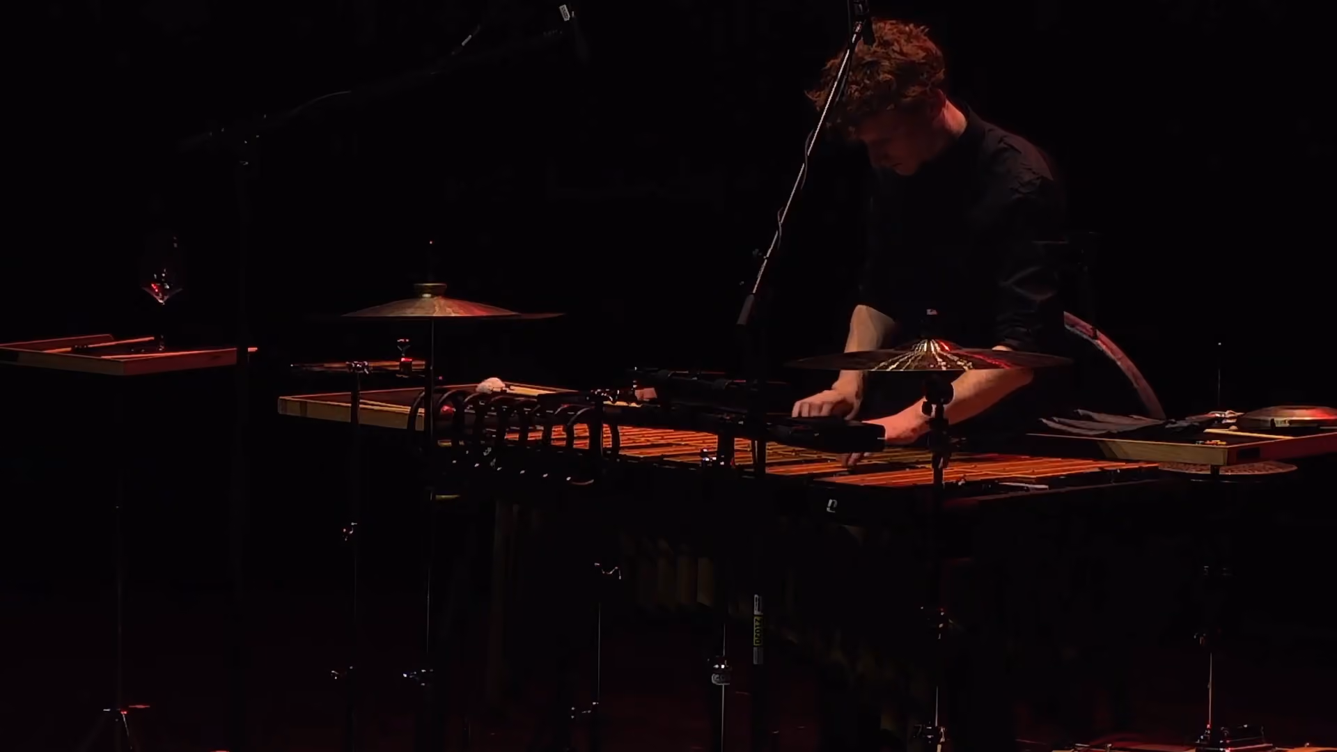 Musicien jouant d'un vibraphone sur scène dans une lumière tamisée, avec un microphone suspendu au-dessus.