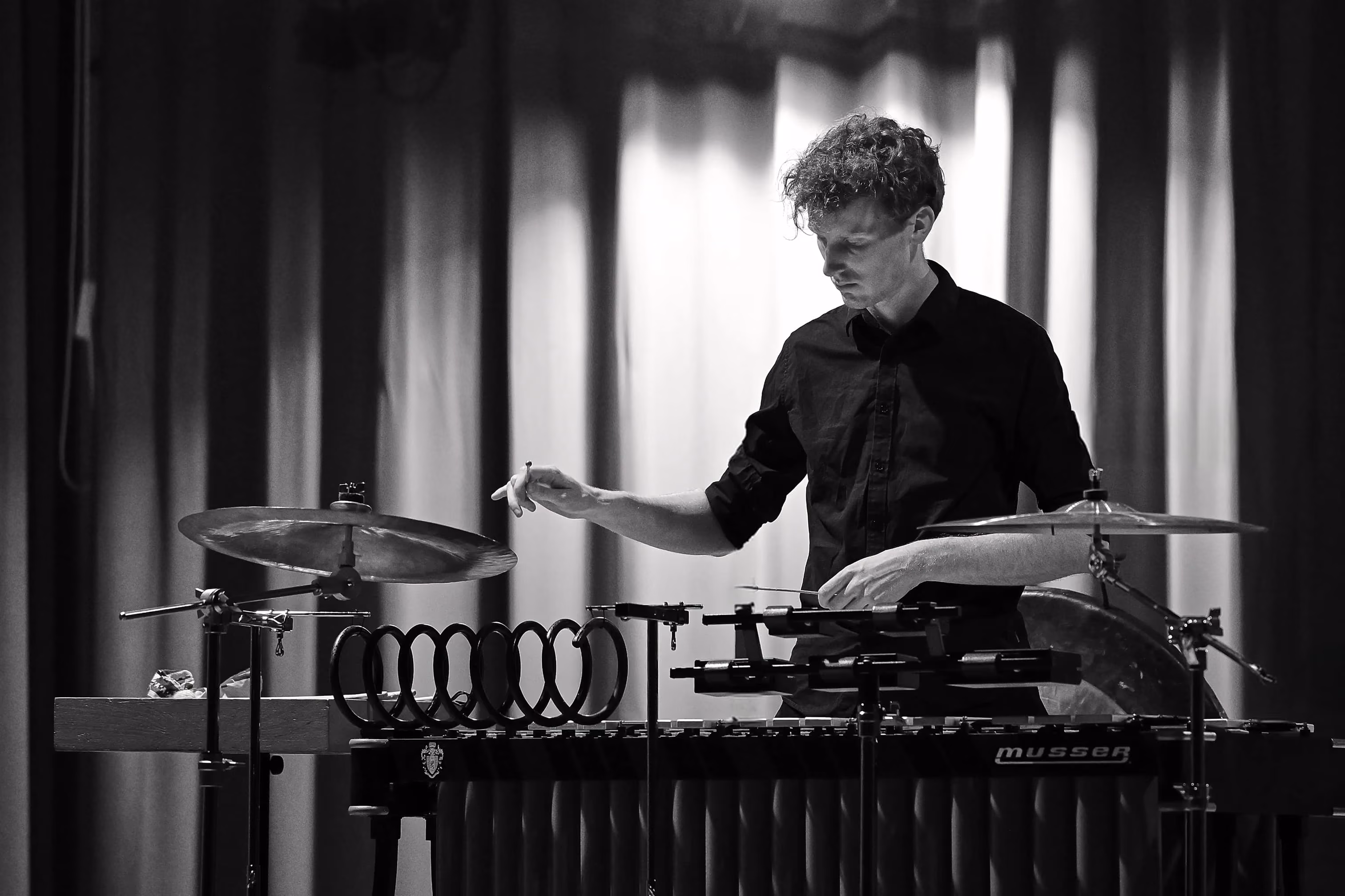 Un musicien jouant du vibraphone avec des cymbales sur chaque côté dans une ambiance de scène avec rideaux en arrière-plan.