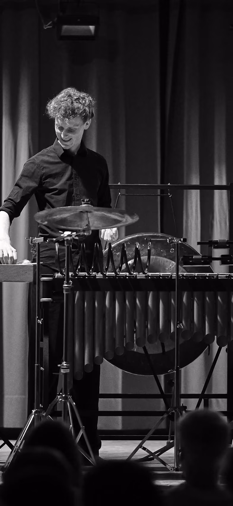 Un musicien jouant du vibraphone sur scène, habillé en noir, dans un décor avec rideaux, éclairage en noir et blanc.