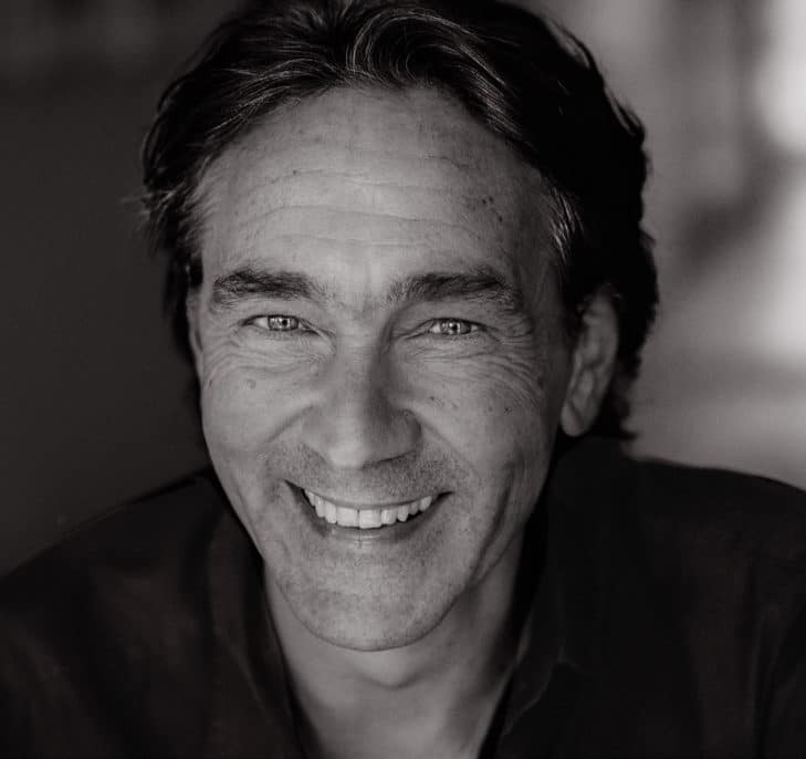 Black and white close-up portrait of a middle-aged man with dark hair smiling directly at the camera.