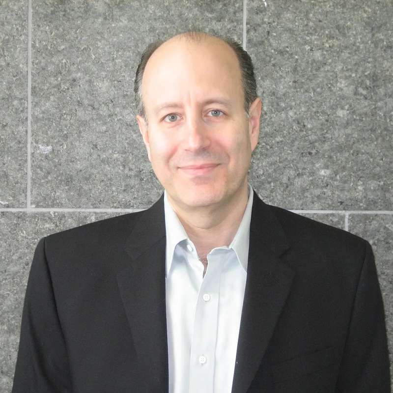 Portrait of Philip Lieberman, Founder and President of Analog Informatics Corporation, in a dark suit jacket and light blue shirt against a gray stone wall.