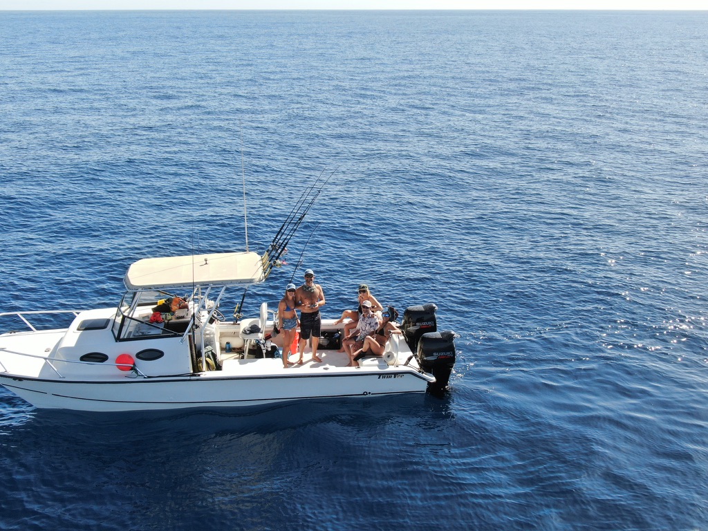 A group aboard a white centre-console fishing boat on flat deep blue water offshore