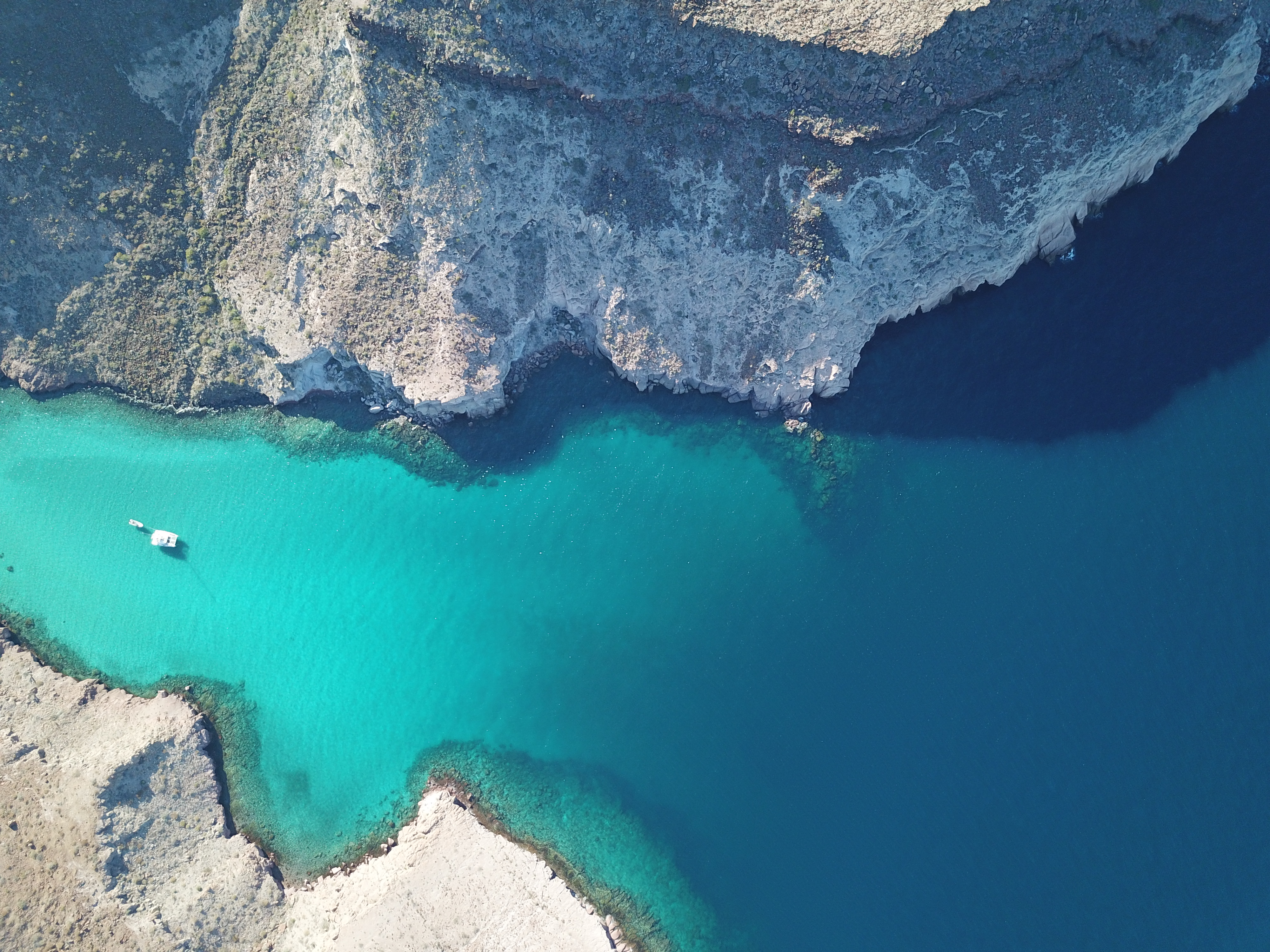 Small boat anchored in a turquoise cove beside pale cliffs