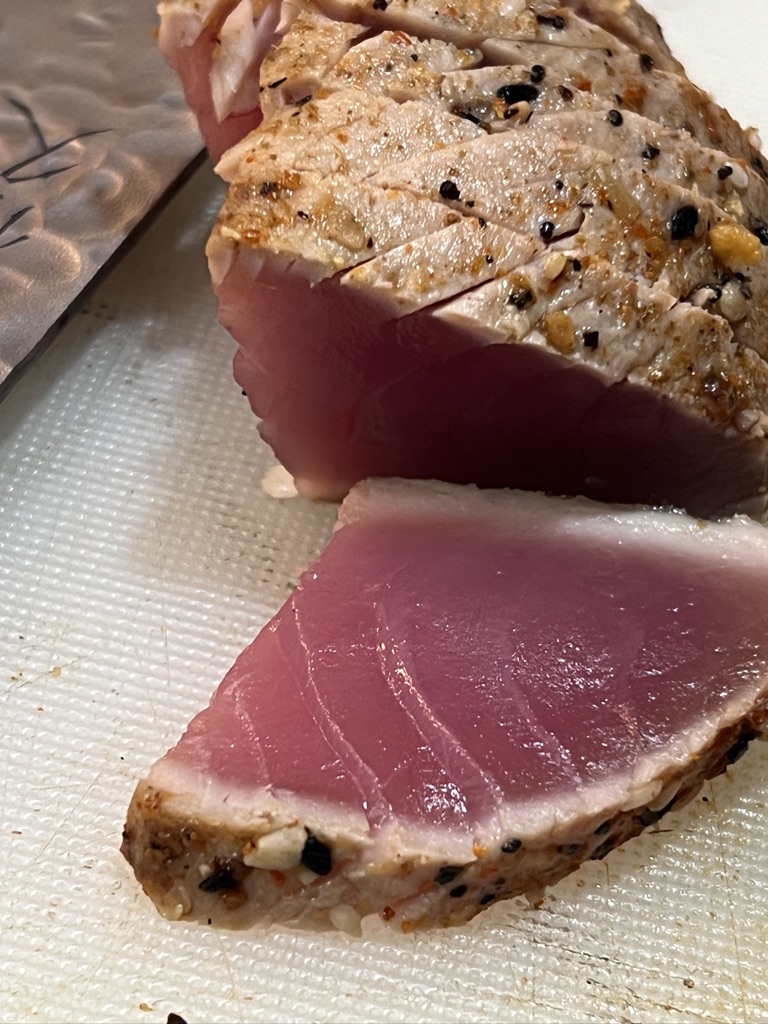 A close-up of a peppered seared tuna loin sliced open to show its deep pink raw centre on a cutting board.