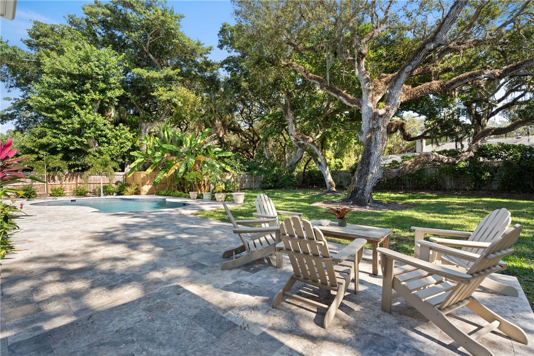 Backyard featuring a stone-paver patio, curved swimming pool, grass lawn, and mature canopy trees