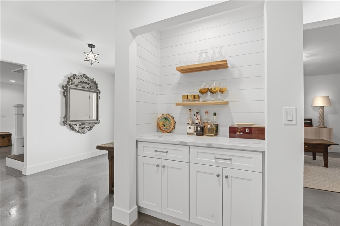 Built-in wet bar featuring white shaker-style cabinetry, a light-toned countertop, horizontal shiplap wall paneling, and two wood-finished floating shelves