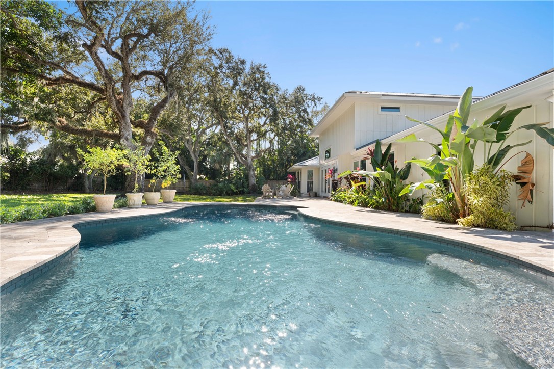 In-ground swimming pool with stone-style decking, white vertical siding exterior, and mature canopy trees