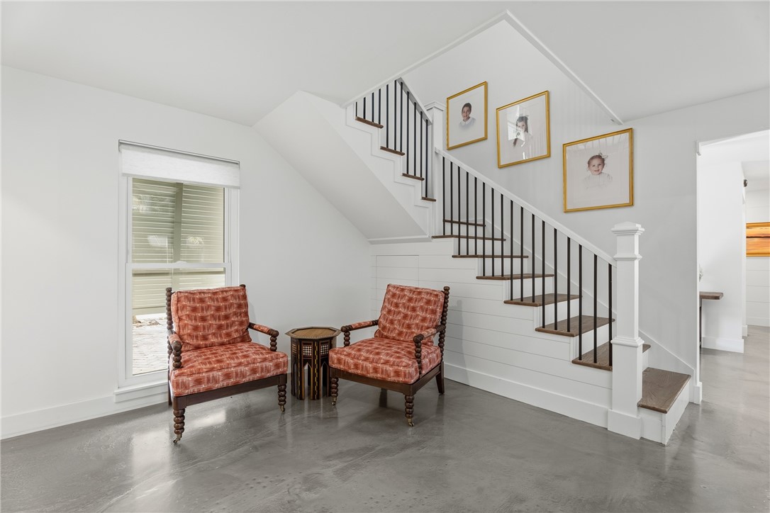 Staircase featuring wood treads, white shiplap wall paneling, and a black metal spindle railing with a white newel post, finished with polished concrete flooring
