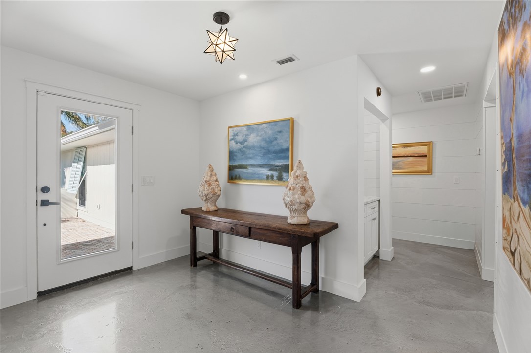 Entry featuring polished concrete flooring, multi-paneled glass entry door, star-shaped geometric light fixture, and horizontal plank wall detailing