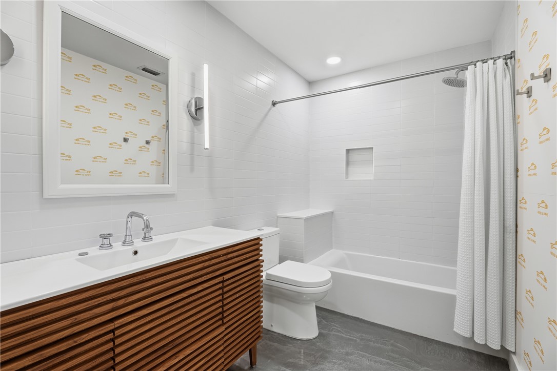Wall-mounted wood-slat vanity with a white countertop and integrated sink, recessed shower niche, vertical LED wall sconce, and large-format tile flooring