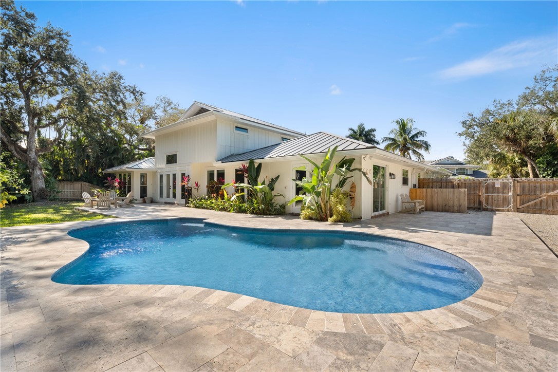 Outdoor living area featuring a free-form swimming pool, extensive stone-tile decking, metal roof, board-and-batten siding, and mature landscaping