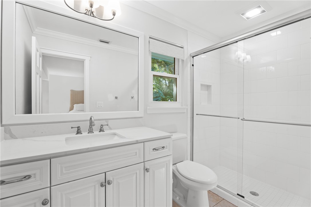Bathroom featuring a white vanity with integrated basin, quartz-style countertop, expansive wall-mounted mirror, and walk-in shower with tiled surround and glass sliding doors