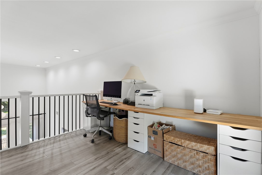 Built-in wood-finish countertop desk with integrated white cabinetry, recessed ceiling lighting, and metal spindle railing