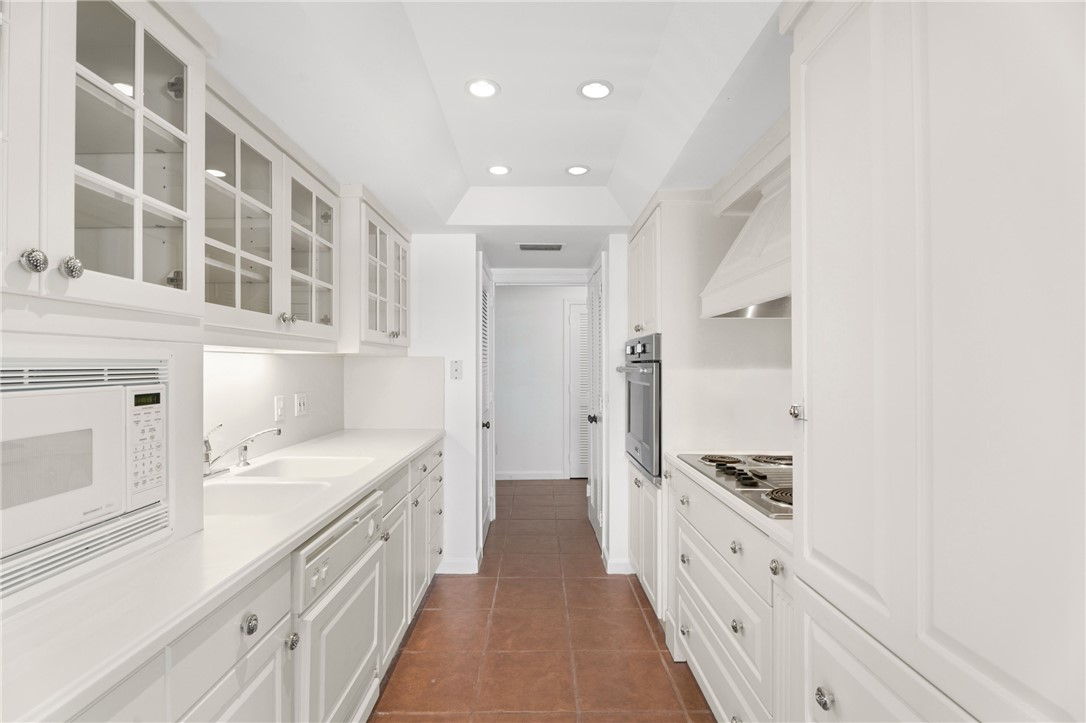 Galley kitchen featuring white cabinetry, integrated appliances, recessed lighting, double basin sink, and tile flooring