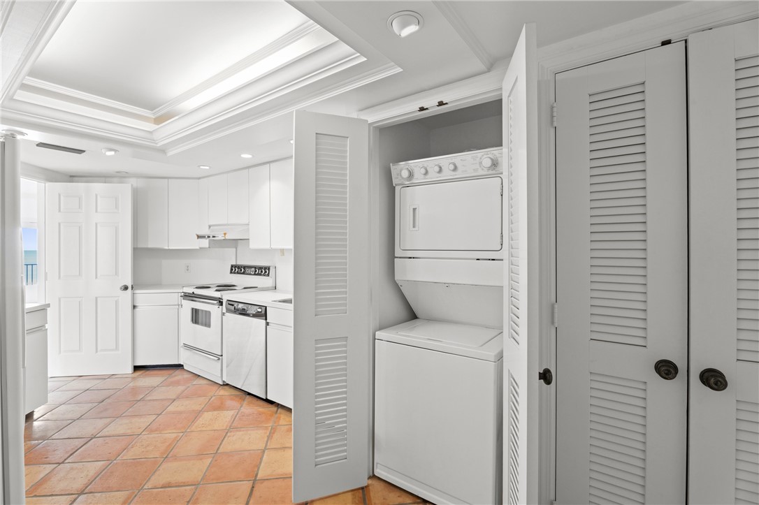 Kitchen space featuring terra cotta style flooring, white cabinetry, and a stacked washer and dryer unit concealed by louvered bi-fold doors