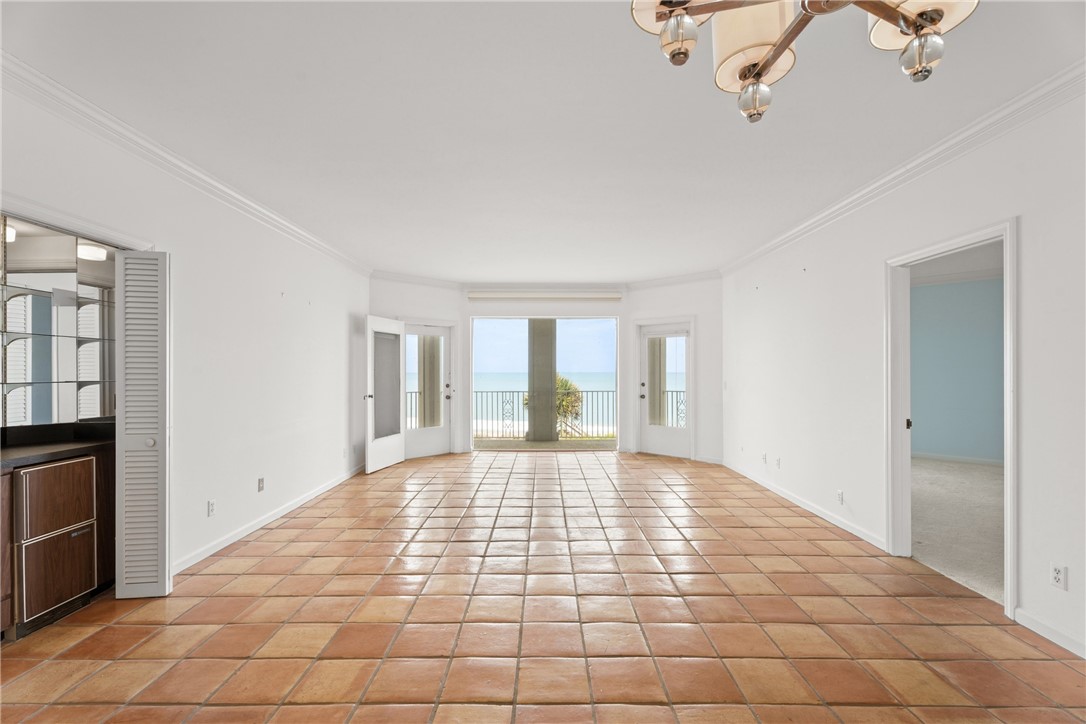 Spacious living area featuring terra cotta tile flooring, crown molding, and direct access to an outdoor balcony