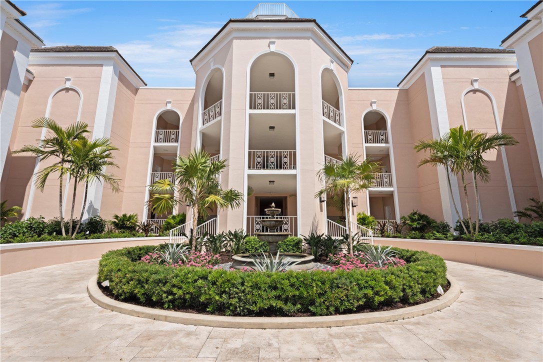 Grand entrance featuring a circular drive with a central fountain, lush landscaping, arched entryways, multi-level balconies with decorative railings, and a domed architectural element